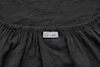 A close-up of a gathered black fabric, possibly a fitted sheet, with a white care label featuring two laundry symbols, partially visible at the seam.
