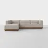 A modern, L-shaped sectional sofa with light beige upholstery and a low wooden base, set against a plain white background.