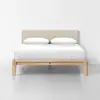 A modern bed with a light wood frame, upholstered beige headboard, and neatly made white bedding with two pillows, set against a plain white wall and floor.