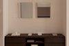 A minimalist room with a dark wood sideboard, books, and decor items. Above the sideboard, two abstract, geometric art pieces hang on a light beige wall. The setting feels calm and organized.