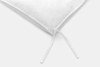 Close-up of the corner of a white pillow with two fabric ties hanging down against a plain light background.