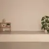 A person practices yoga in a minimal room with a shelf, plants, and a lamp, performing various poses on a light-colored mat. The setting is calm and serene.