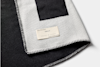 A close-up of a folded black and white woven blanket with a stitched-on label reading Edition 01 and blank lines for numbering, highlighting the blankets texture and stitching details.