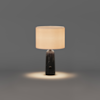 Table lamp with a dark, cylindrical marble base and a cylindrical fabric shade casting a warm light onto the surface below.