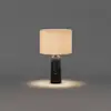 Table lamp with a dark, cylindrical marble base and a cylindrical fabric shade casting a warm light onto the surface below.