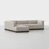 A modern L-shaped sectional sofa with light beige upholstery and a dark wooden base, set against a plain white background.