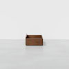 A small, rectangular wooden box with short legs, placed on a smooth, light gray floor against a plain white background.