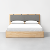 A modern wooden bed with a light wood frame, a gray cushioned headboard, and white bedding with two pillows, set against a plain white wall and gray floor.