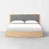 A modern wooden bed with a light wood frame, a gray cushioned headboard, and white bedding with two pillows, set against a plain white wall and gray floor.