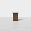 A wooden rectangular table with a flat, light-colored top and a solid, darker rectangular base, standing on a plain white floor against a white background.