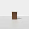 A wooden rectangular table with a flat, light-colored top and a solid, darker rectangular base, standing on a plain white floor against a white background.