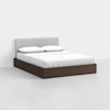 A modern bed with a light gray upholstered headboard, white bedding, and a dark brown wooden frame, positioned against a plain white wall on a light-colored floor.