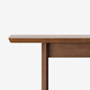 Close-up of the edge and leg of a wooden table with a smooth finish, set against a plain white background.