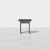 A simple, modern wooden stool with a dark padded seat, photographed against a plain white background.