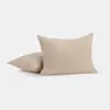 Two beige, textured pillows are placed on a plain white background. One pillow stands upright, while the other lies flat behind it.