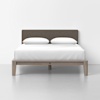 A neatly made bed with a wooden frame, gray upholstered headboard, white sheets, and two white pillows, set against a plain white background.