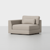 A modern, light beige upholstered corner chair with a square shape, low backrest, and matching rectangular cushion, shown against a plain white background.