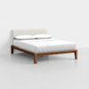 A modern wooden bed frame with a light upholstered headboard, dressed in white bedding and two white pillows, set against a plain white background.