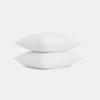 Two plain white pillows are stacked neatly on top of each other against a white background.