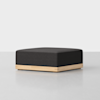 A square, black upholstered ottoman with a light wood base, set on a smooth, light gray surface against a plain white background.