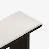 A close-up view of the corner of a bench with a cushioned, light-colored upholstered seat and a dark wooden frame against a white background.