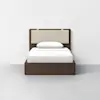 A modern twin bed with a dark wooden frame, beige upholstered headboard, and white bedding, including a pillow and neatly made sheets, set against a plain white wall and light gray floor.