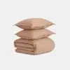 Two beige pillows stacked on top of a neatly folded beige comforter, all placed against a plain white background.