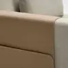 Close-up of a light grey upholstered chair with a tan leather armrest cover featuring a side pocket. The image highlights the texture and materials of the chair and cover.