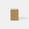A modern wooden nightstand with a minimalist cube design, featuring an open shelf at the bottom and a single drawer that is partially pulled out. The nightstand sits on a plain, light-colored floor against a white background.