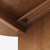 Close-up view of the underside of a wooden table, showing a joining corner with a black screw or bolt securing the pieces together. The wood has a smooth, polished brown finish.