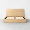 A modern wooden platform bed frame with a tall rectangular headboard and slatted base, set against a plain white wall on a smooth gray floor.