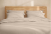 A neatly stacked set of beige bed linens, including folded sheets and pillowcases, displayed against a white background.