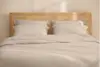 A neatly stacked set of beige bed linens, including folded sheets and pillowcases, displayed against a white background.
