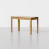 A simple wooden table with a rectangular top and four straight legs, placed on a smooth, light gray floor against a plain white background.