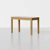 A simple wooden table with a rectangular top and four straight legs, placed on a smooth, light gray floor against a plain white background.