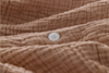 A close-up of a textured brown fabric with a single white, four-hole button sewn onto it. The fabric appears soft and crinkled, creating gentle folds and shadows around the button.