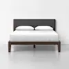 A modern bed with a dark wooden frame, a dark gray upholstered headboard, and white bedding with two pillows, positioned against a white wall in a minimalistic setting.