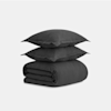 Two dark gray pillows stacked on top of a neatly folded matching dark gray duvet against a plain light gray background.