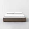 A neatly made bed with a gray upholstered frame, white bedding, and two white pillows, set against a plain white wall and a light gray floor.