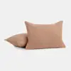Two light brown, rectangular pillows with a soft, textured fabric are displayed against a plain white background. One pillow stands upright while the other lies flat behind it.