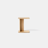 A minimalist wooden stool with a light natural finish, shaped like a capital I, placed on a smooth, light gray floor against a plain white background.