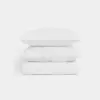 Two white pillows are stacked on top of a folded white comforter, all set against a plain white background. The bedding looks clean, soft, and neatly arranged.