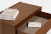 A wooden drawer is partially open with a notebook and pen inside. On top of the drawer, there are two closed books stacked neatly against a plain light background.