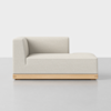 A modern, minimalist light beige chaise lounge with a low backrest and wooden base, set against a plain white background.