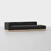 A modern, minimalist black sectional sofa with low backrests, set on a light wooden base, placed in a clean, bright room with a plain white background.