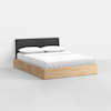 A modern bed with a light wood frame, white bedding, two pillows, and a dark gray upholstered headboard, set against a plain white wall and floor.