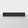 A long, modern sectional sofa with dark upholstery and a low backrest sits on a light, empty floor against a plain white background.