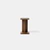A minimalist wooden stool with a rectangular top and base, connected by a central rectangular support, set against a plain white background.