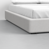 Close-up of a modern, low-profile bed with a light gray upholstered frame and white bedding, set on a smooth, light gray floor in a minimalistic room.