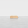 A small, rectangular wooden box sits alone on a smooth, light gray surface against a plain white background.